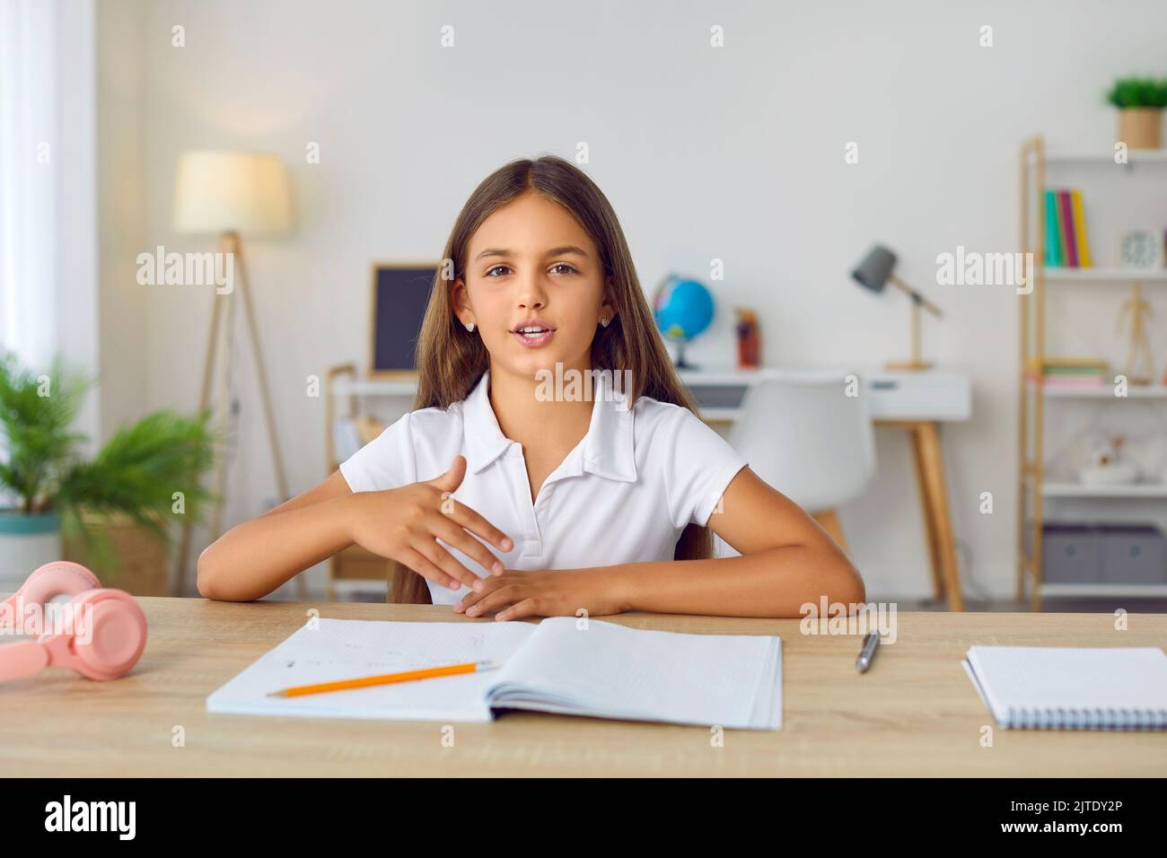 Das Mädchen der Grundschule sitzt zu Hause am Schreibtisch, hat eine Online-Lektion und spricht Stockfoto