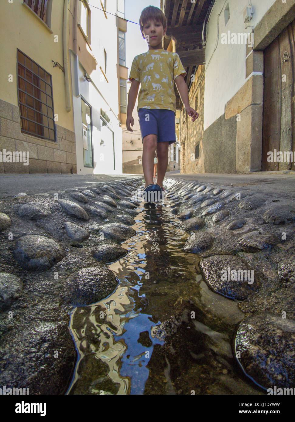 Kind, der am Straßenwasserkanal in Losar de la Vera, Caceres, Extremadura, Spanien, läuft Stockfoto