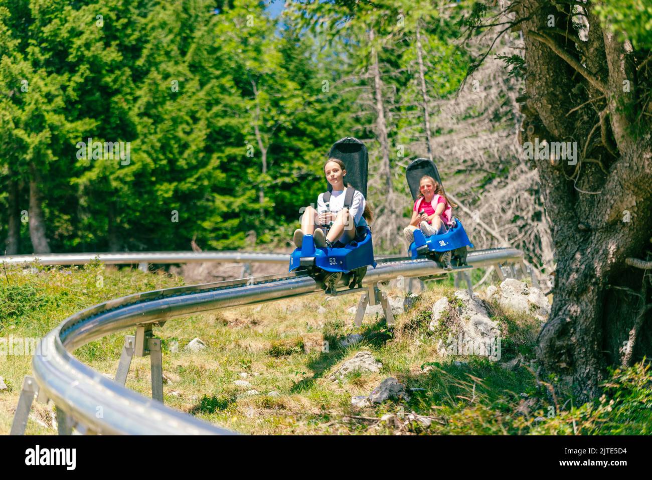 Skigebiet Bergbahn. Zwei Mädchen, eines hinter dem anderen, gehen die Skipiste hinunter. Wald und Bäume im Hintergrund Stockfoto