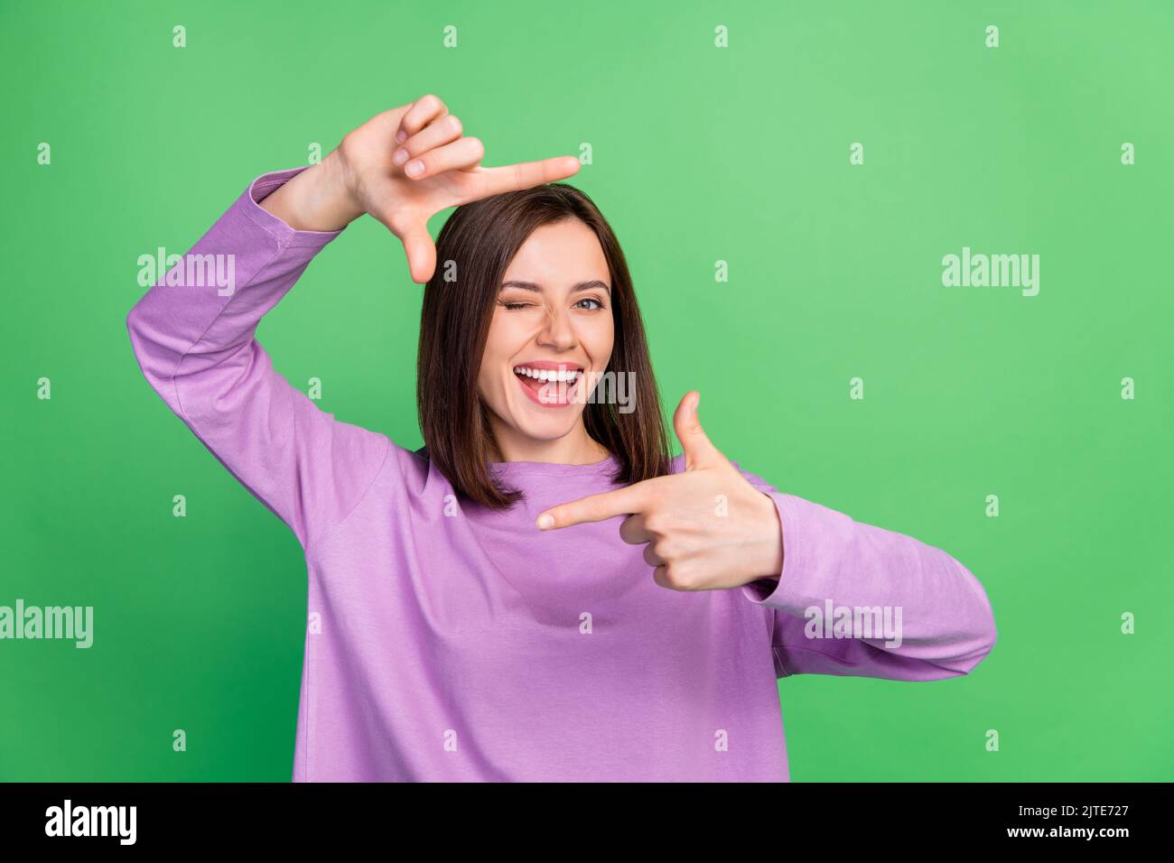 Portrait Foto von jungen attraktiven schönen Mädchen blinkenden Auge halten Finger Kader lächelnd isoliert auf grünem Hintergrund Stockfoto