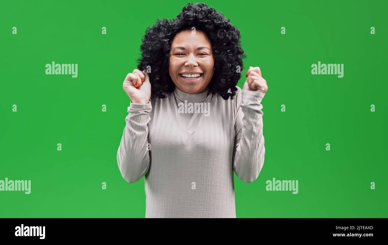 Eine afrikanische Frau mit lockigen Haaren feiert ihren Sieg im Chroma-Key-Hintergrund Stockfoto