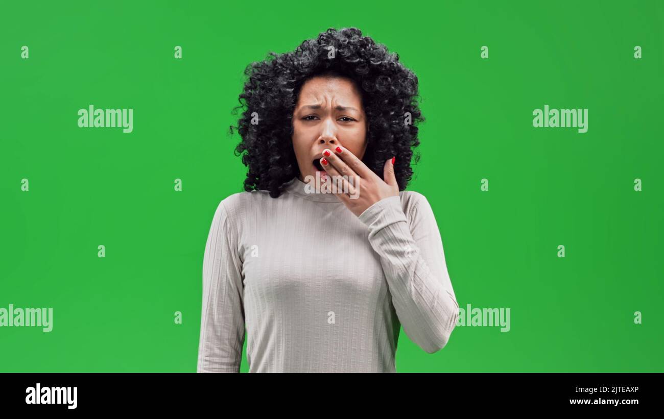 Eine afrikanische Frau mit lockigen Haaren stehend und gähnend im Chroma-Key-Hintergrund Stockfoto