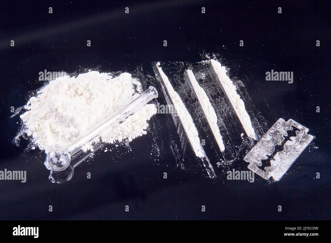 Stapel weißer Puderdrogen und Rauchrohr aus Glas. Rasiermesser- und Kokainlinien zum Schnauben. Stockfoto