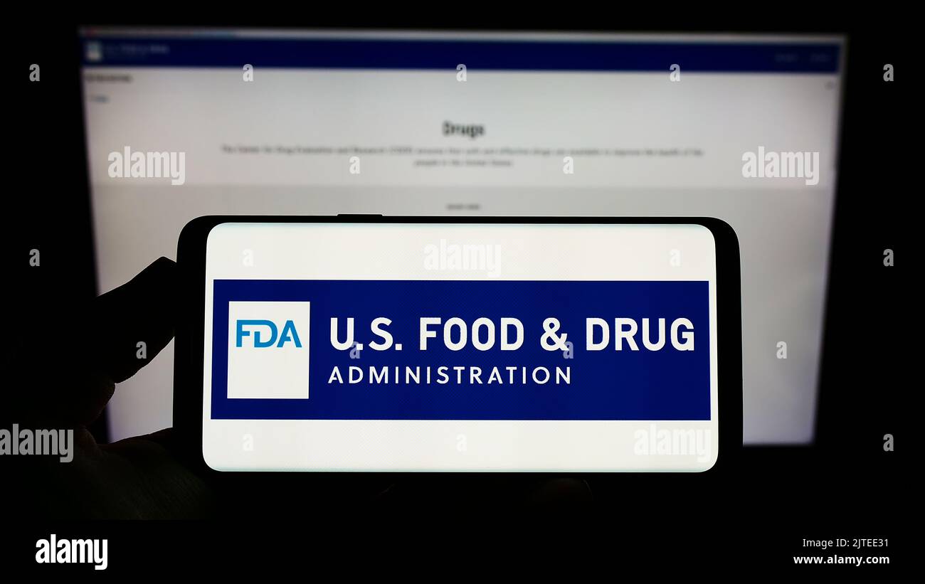 Person, die das Smartphone mit dem Logo der US-amerikanischen Food and Drug Administration (FDA) auf dem Bildschirm vor der Website hält. Konzentrieren Sie sich auf die Telefonanzeige. Stockfoto