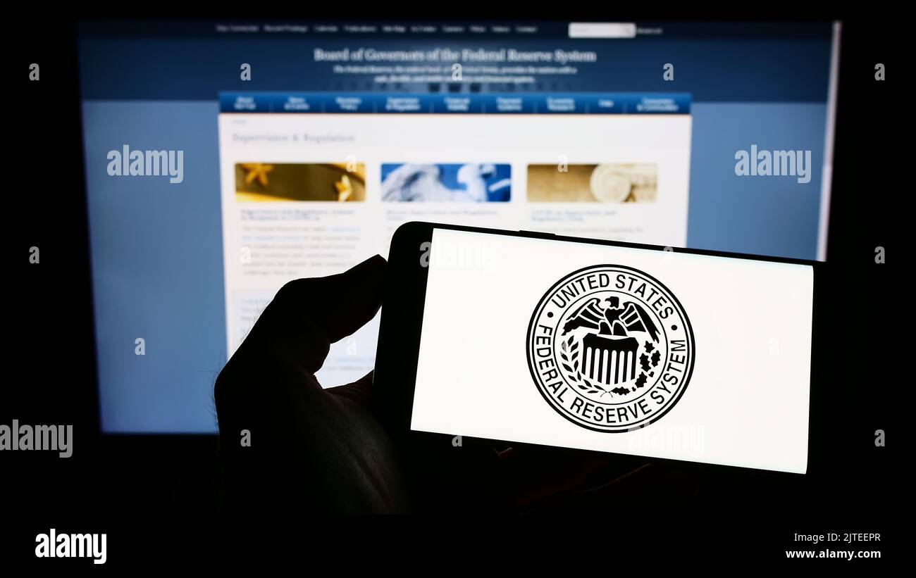 Person, die das Mobiltelefon mit dem Siegel des US-amerikanischen Federal Reserve System (Fed) auf dem Bildschirm vor der Webseite hält. Konzentrieren Sie sich auf die Telefonanzeige. Stockfoto