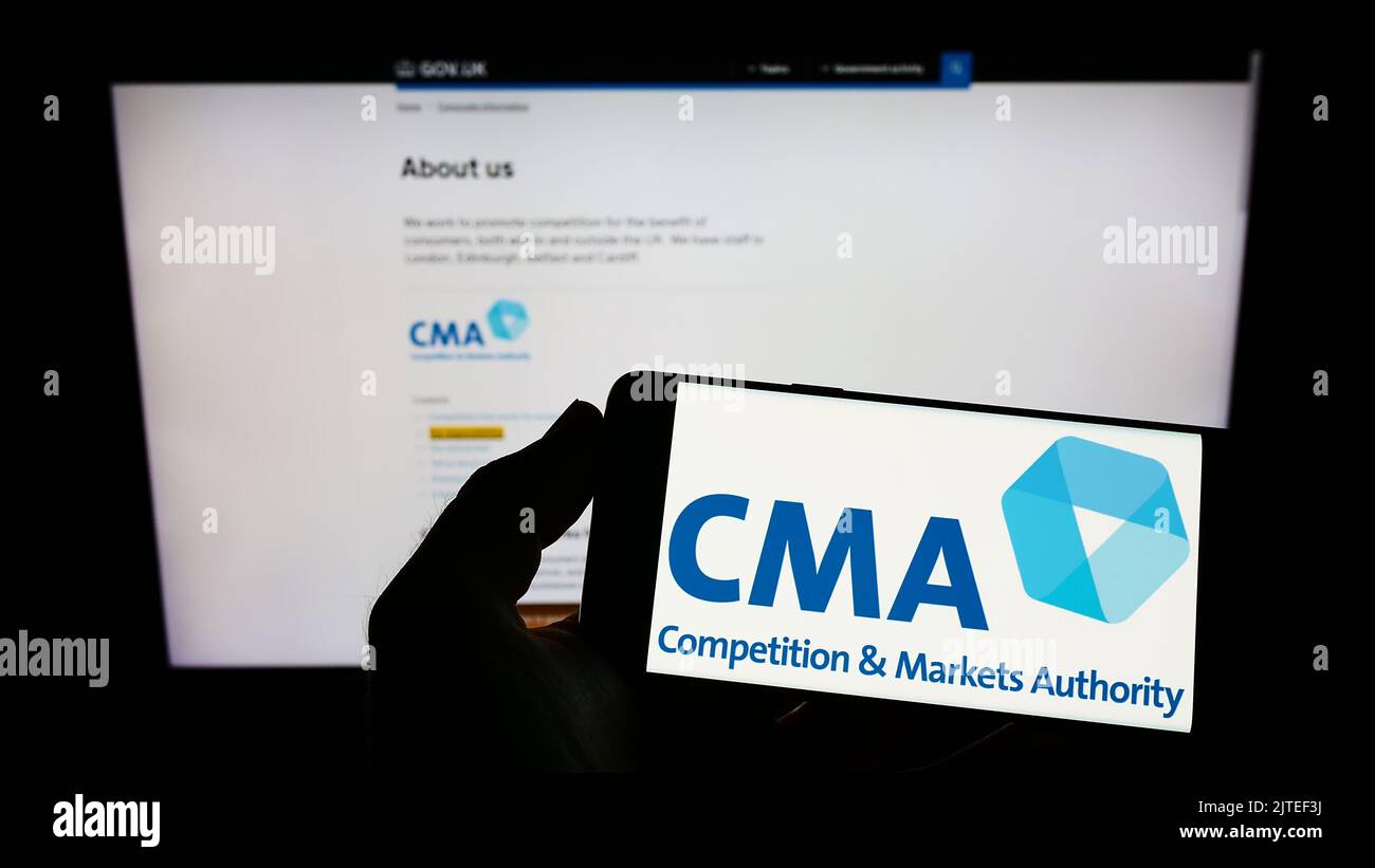 Person, die das Smartphone mit dem Logo der British Competition and Markets Authority (CMA) auf dem Bildschirm vor der Website hält. Konzentrieren Sie sich auf die Telefonanzeige. Stockfoto