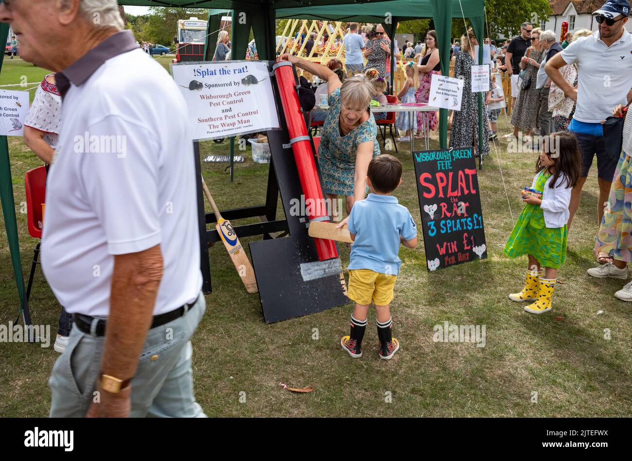 Ein kleiner Junge wird mit einer Fledermaus zum traditionellen Spiel „Splat the Rat“ im Wisborough Green Village Fete in West Sussex, Großbritannien, überreicht. Stockfoto