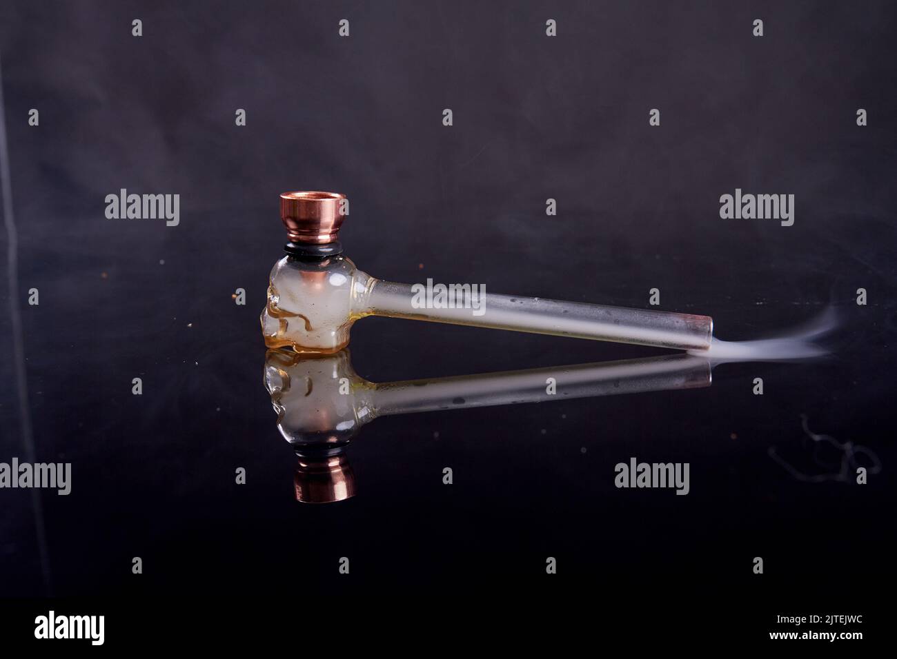 Glasrohr für Risse oder Kristallmeth auf reflektierender Spiegelfläche. Rauch auf schwarzem Hintergrund. Stockfoto