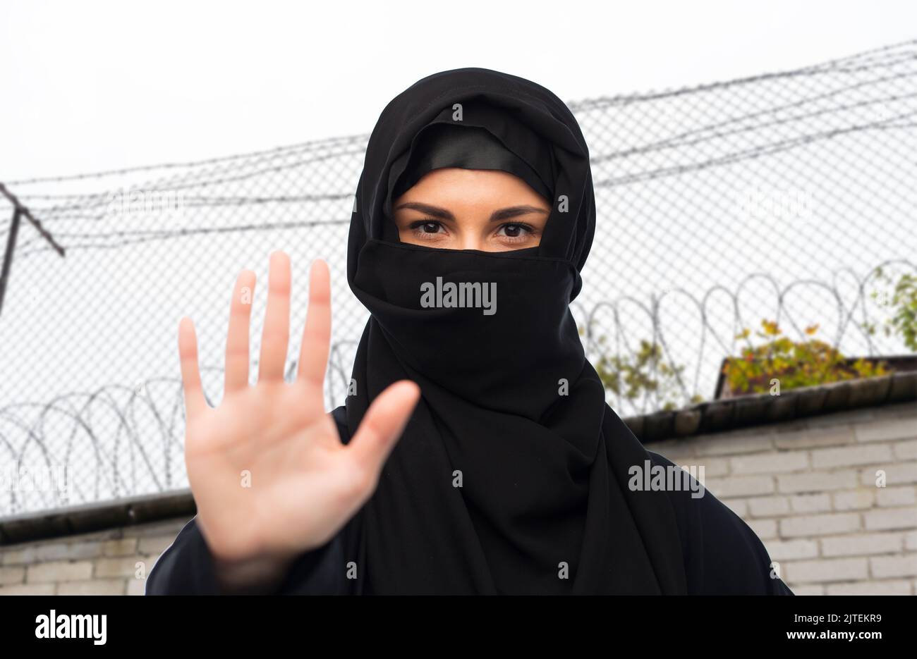 Frau in Hijab zeigt Stoppschild über Stacheldraht Stockfoto