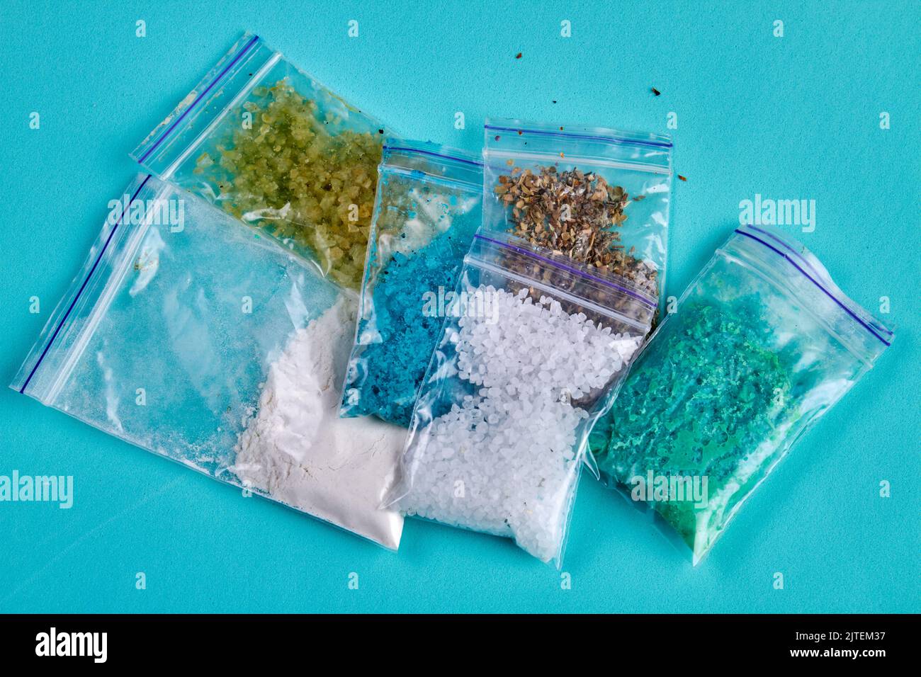 Plastikpakete mit verschiedenen bunten Drogen. Isoliert auf blauem Hintergrund. Stockfoto