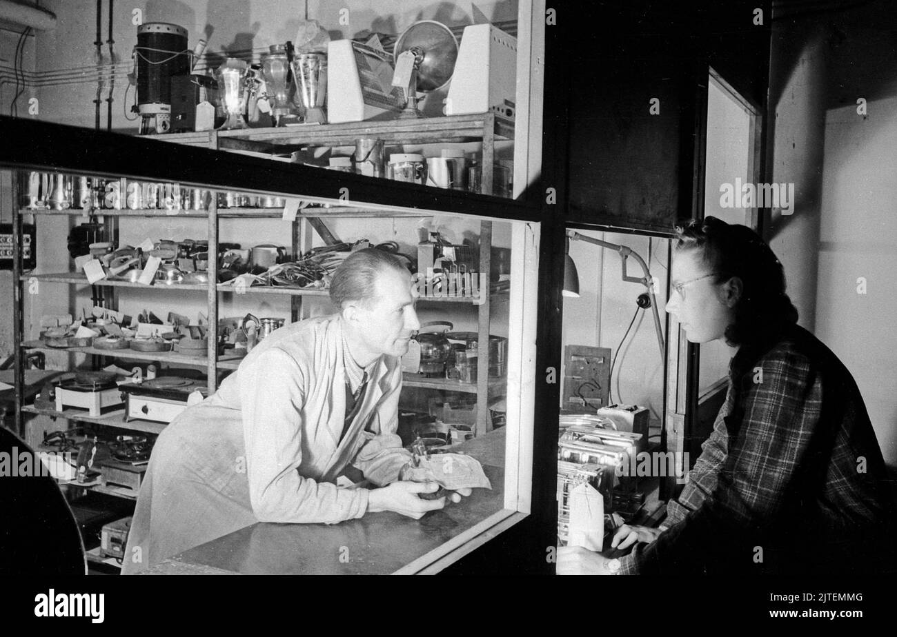 Kundin auf der Suche nach passenden Ersatzteilteilen für ihr Elektrogerät in der Siemens-Werkstatt, Berlin, Deutschland 1947. Stockfoto