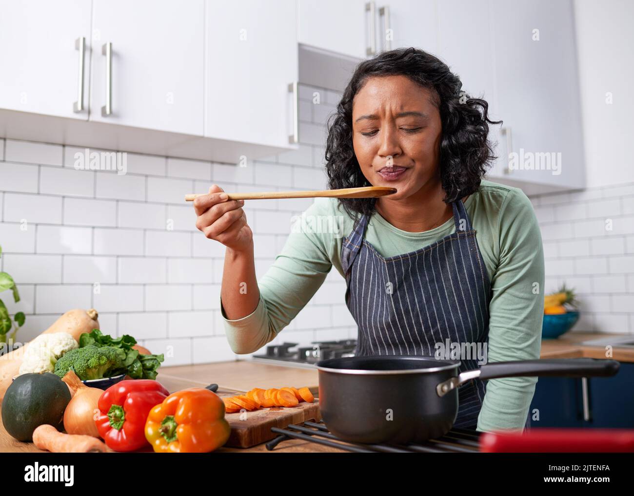Eine junge Frau aus verschiedenen Rassen schmeckt ihre Küche und ist unsicher über den Geschmack Stockfoto