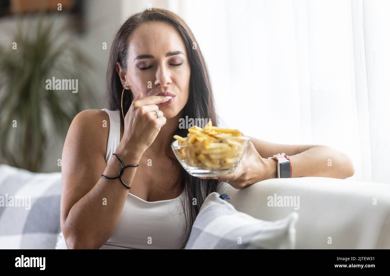 Frau leckt sich den Finger und genießt den Geschmack knuspriger und weicher frischer pommes Frites. Stockfoto
