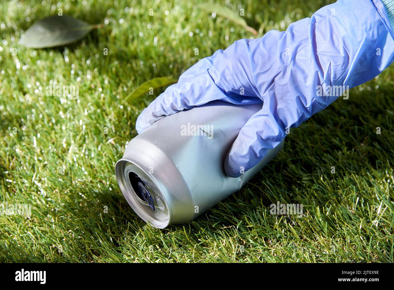 Nahaufnahme der Hand im Handschuh mit gebrauchter Dose auf Gras Stockfoto