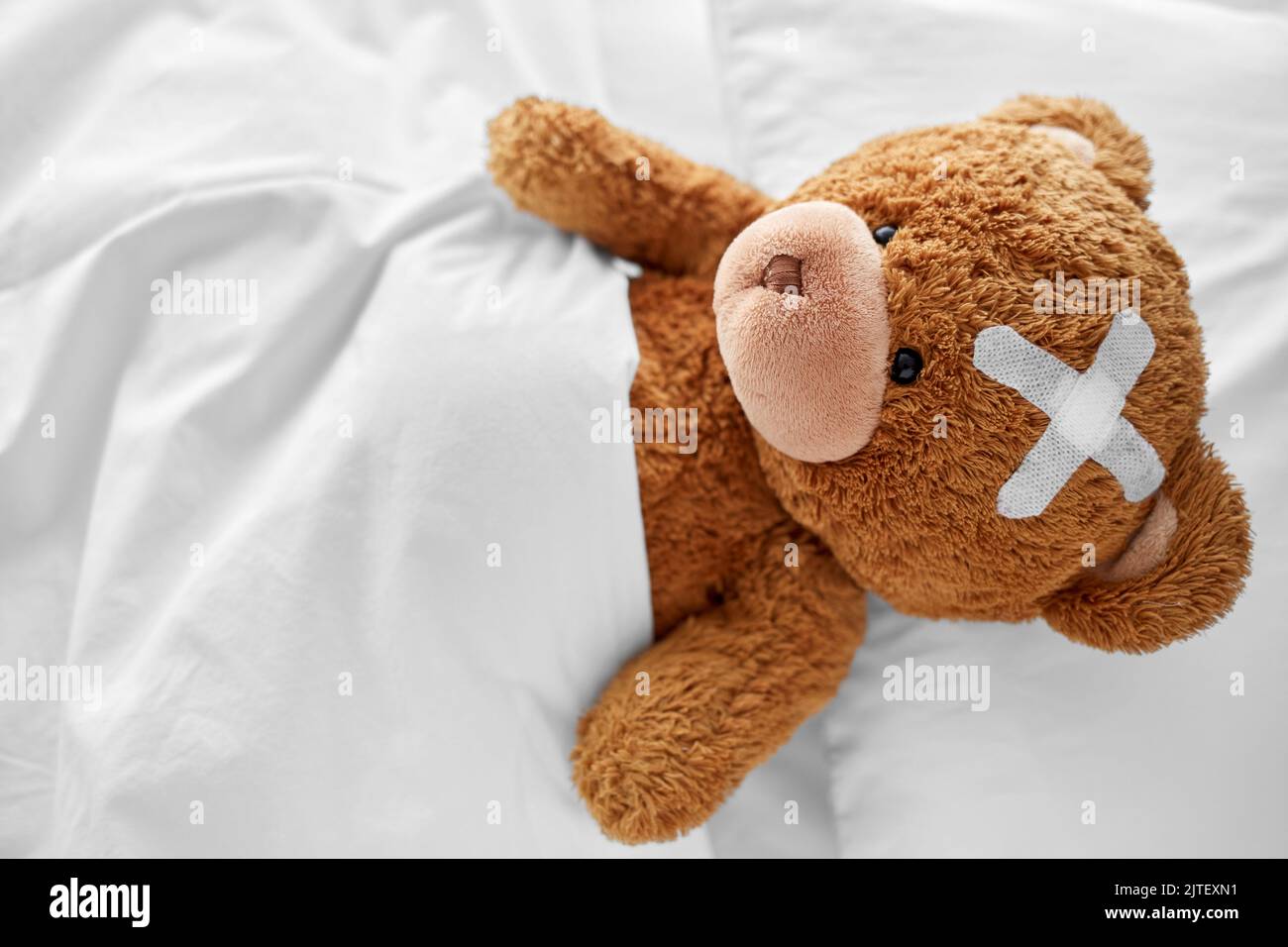 teddybär mit einem medizinischen Pflaster auf dem Kopf, der im Bett liegt Stockfoto