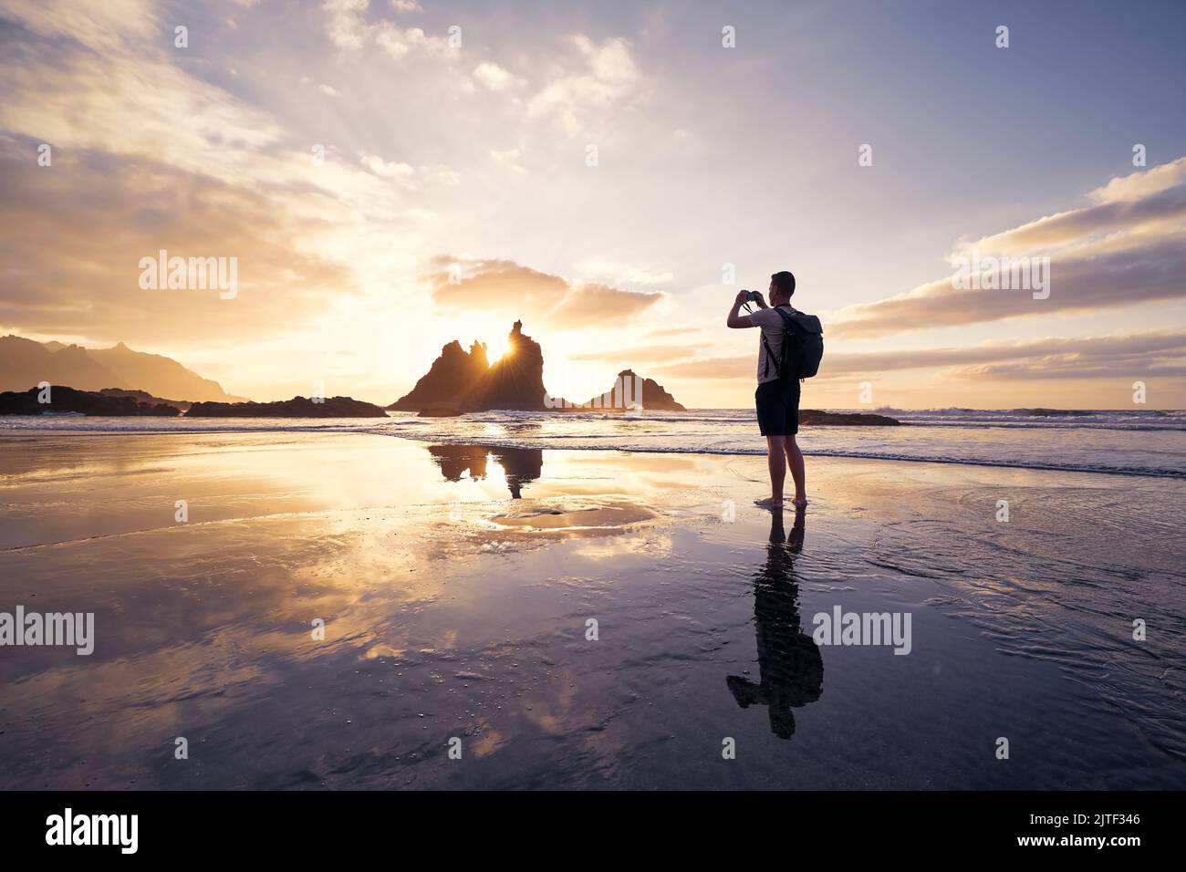 Mann beim Fotografieren von Landschaft mit Klippe. Fotograf am Strand bei schönem Sonnenuntergang. Teneriffa, Kanarische Inseln, Spanien. Stockfoto
