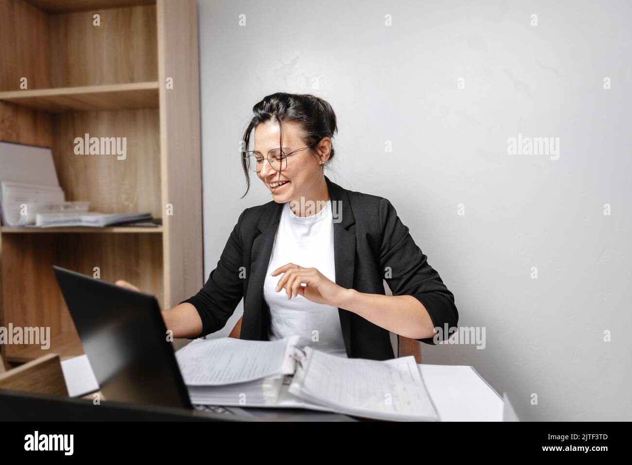 Lächelndes junges Mädchen, das im Büro arbeitet. Fröhlicher, hübscher Student mit gemischter Rasse, der einen Computerbildschirm betrachtet, ein Webinar oder eine Online-Studie anschaut Stockfoto