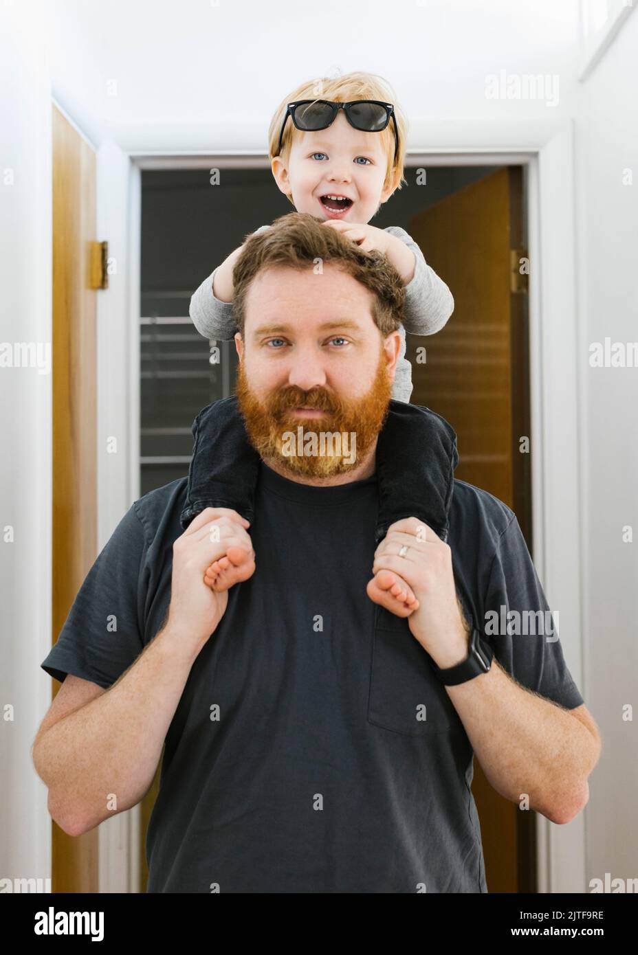 Das Porträt eines Vaters, der seinen Sohn (2-3) zu Hause auf den Schultern trägt Stockfoto