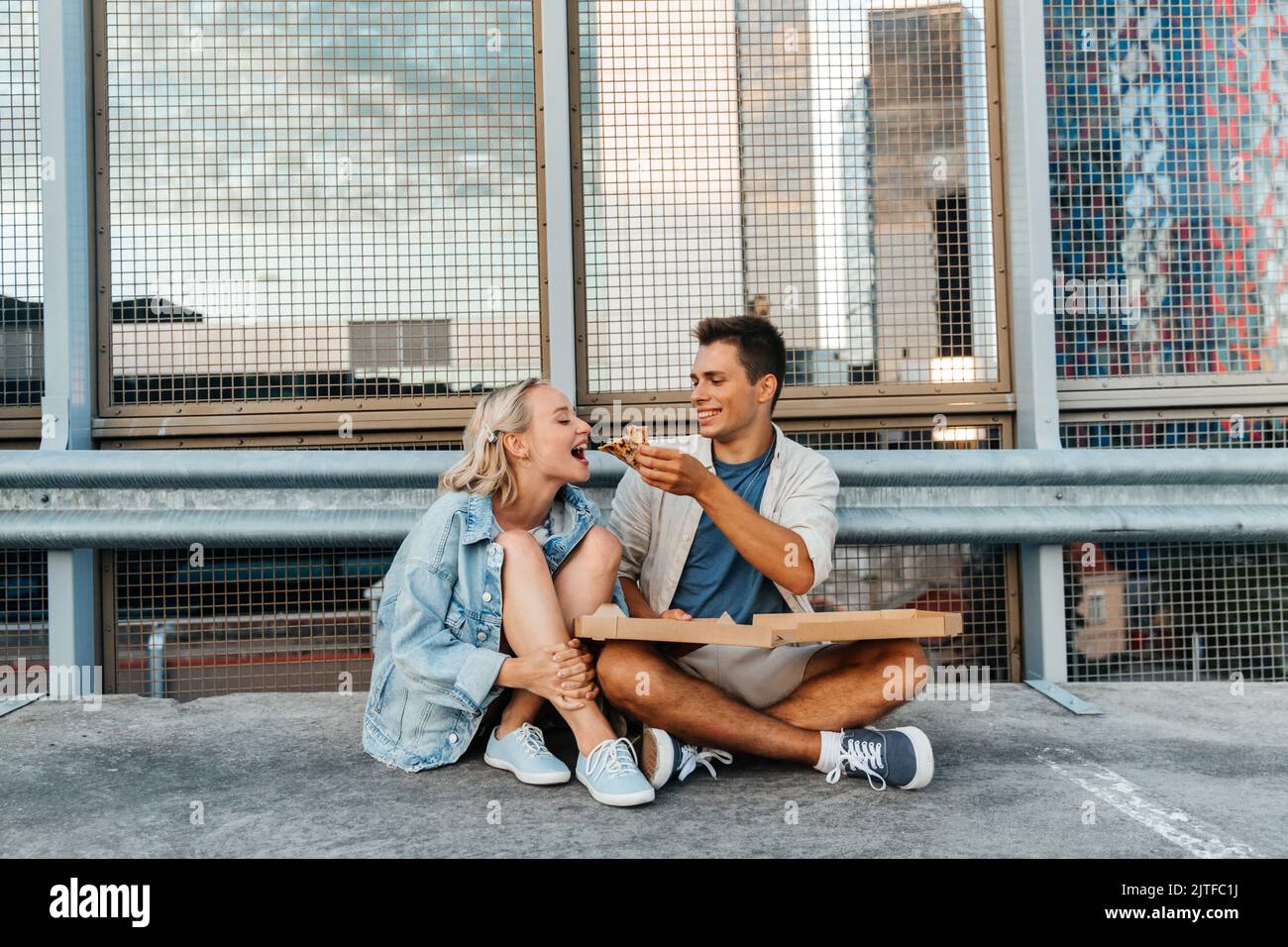 Ein glückliches Paar, das auf dem Parkplatz auf dem Dach der Stadt Pizza gegessen hat Stockfoto