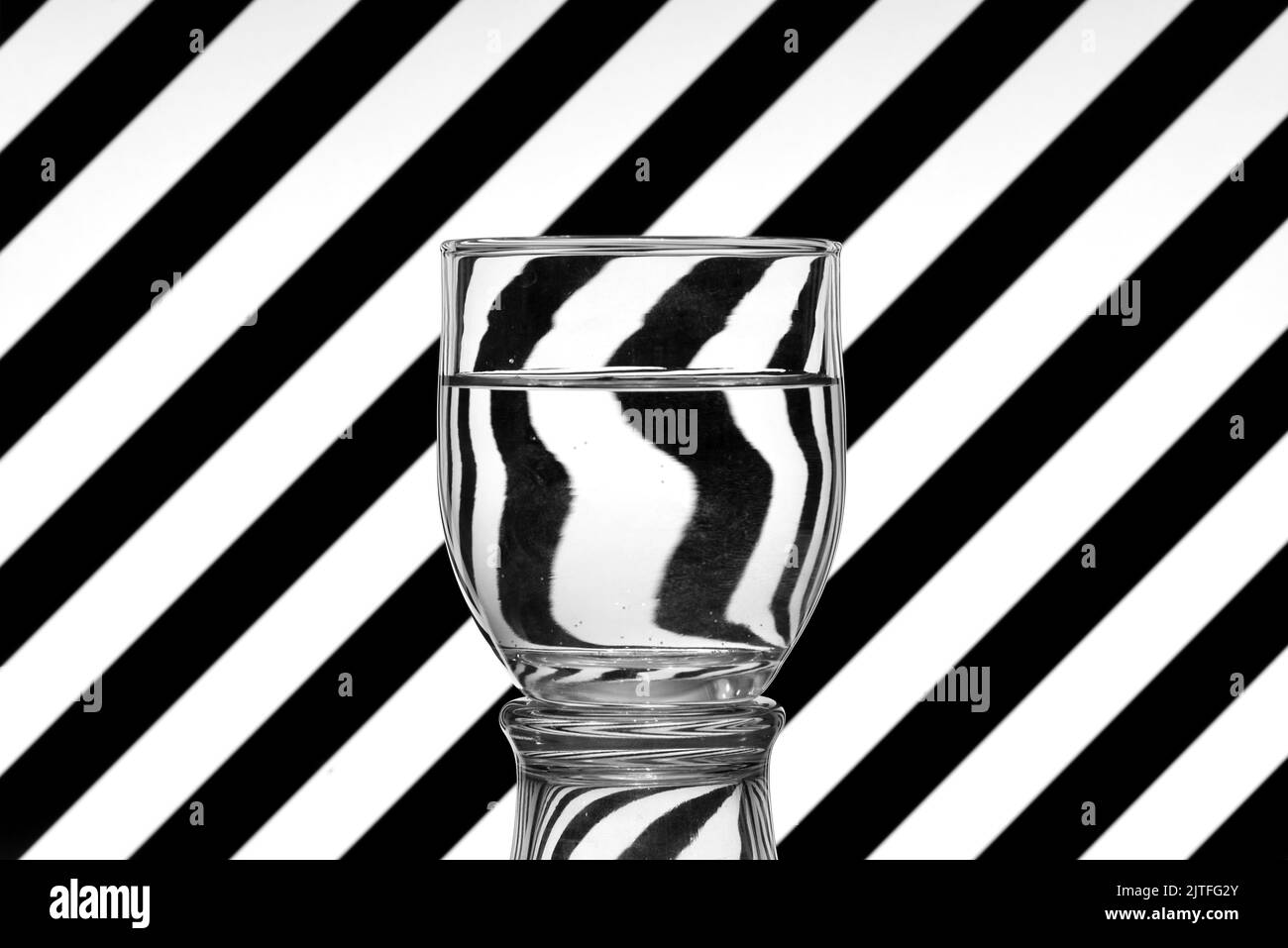 Ilusión óptica creada mediante la refracción de la luz, lineas oblicuas en Blanco y Negro reflejadas en un vaso de agua Stockfoto