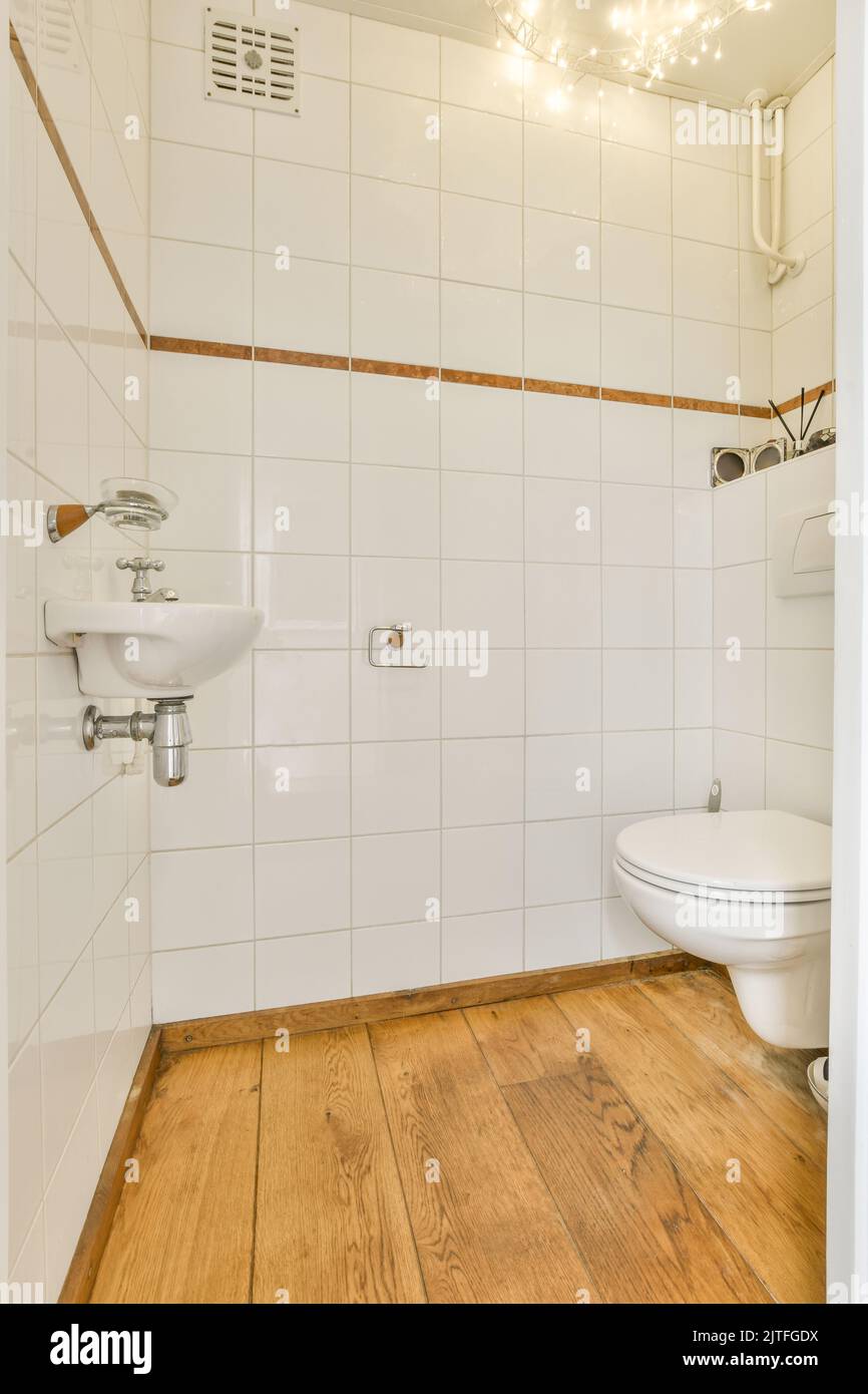 Toilette an der Wand und kleines Waschbecken im Waschraum mit weißen Fliesen Stockfoto