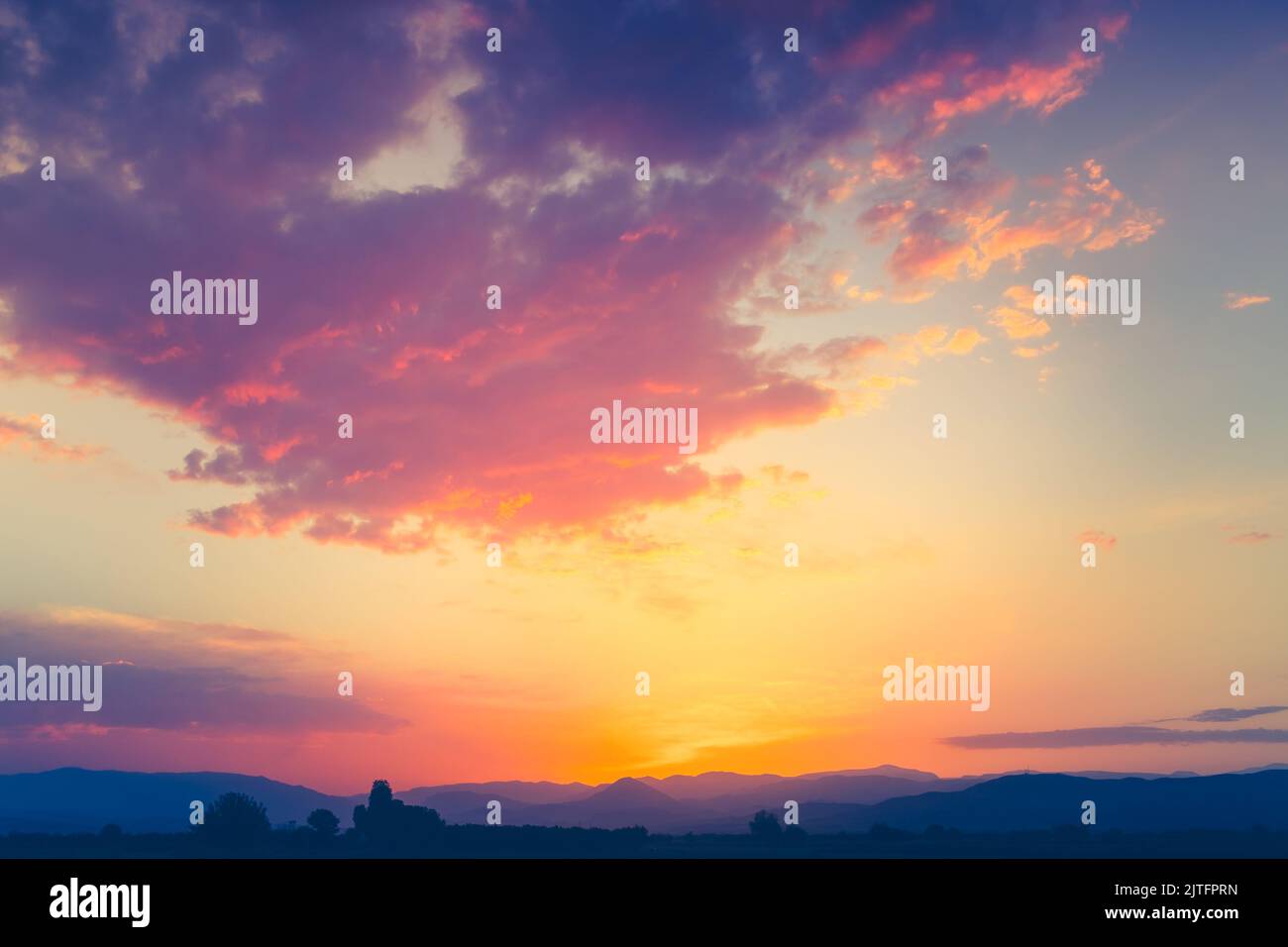 Farbenfroher Sonnenuntergang am Himmel mit hellen Wolken und Bergkette im Hintergrund. Atemberaubende natürliche Sommerabendszene. Stockfoto