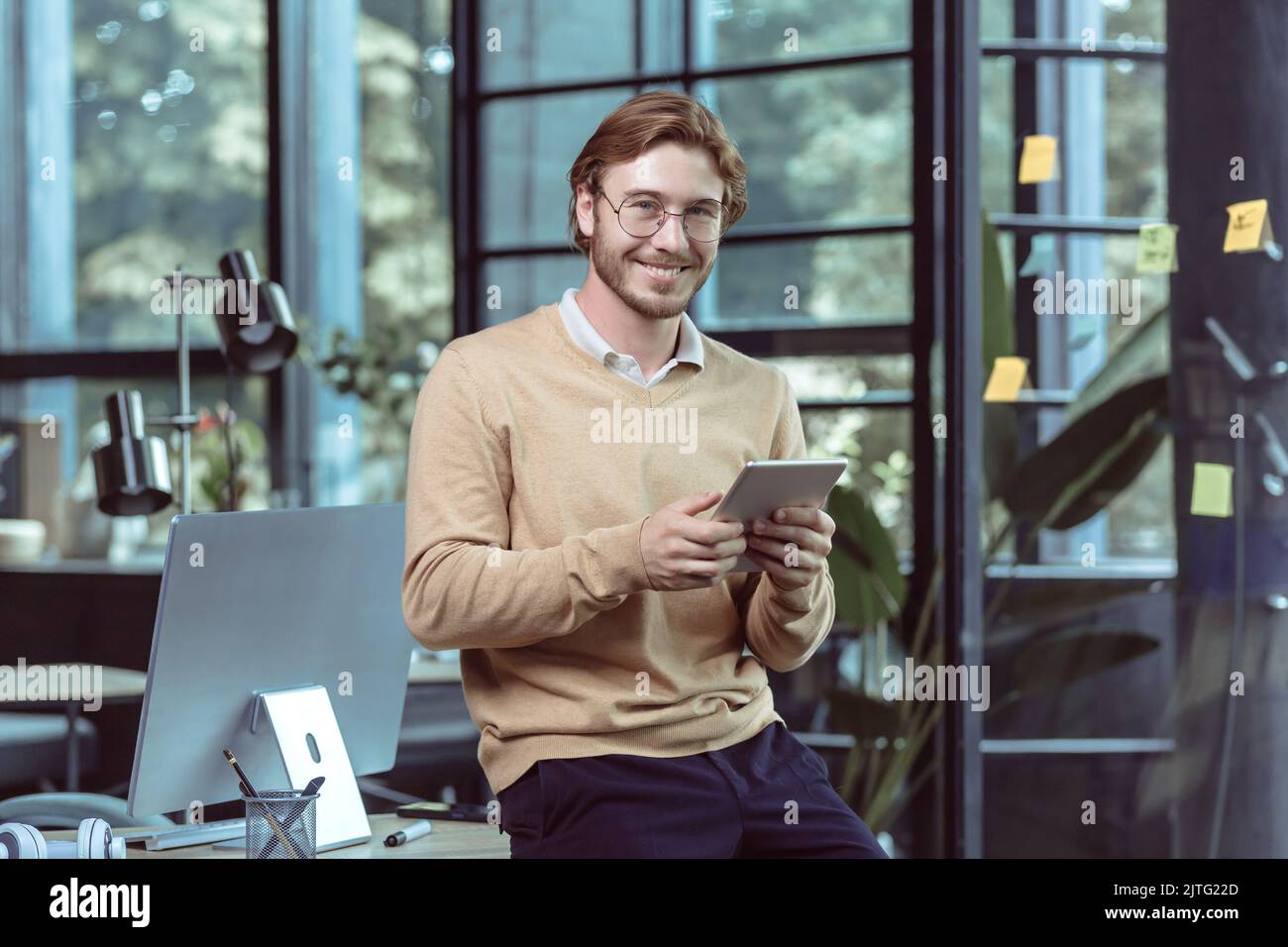 Portrait des jungen Geschäftsmannes Geschäftsmann Mann blonde lächelnd und Blick auf die Kamera, bei der Arbeit in modernen Loft-Büro, mit Tablet-Computer, IT-Spezialist testen neue Software-Anwendung Stockfoto