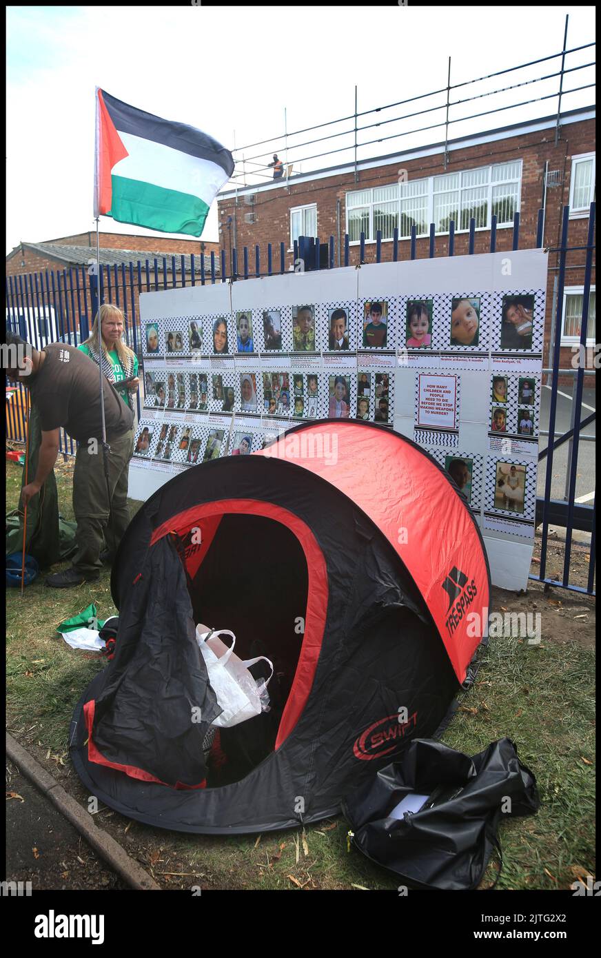 Demonstranten schlagen ihre Zelte auf, beobachtet von einem Polizeibüro, vor einer Ausstellung von Fotos von kürzlich getöteten Kindern in Gaza, während sich Anhänger der Palästina-Aktion mit anderen Protestgruppen zusammentaten, um vor UAV-Triebwerken, Schepstone und Mitarbeitern zu demonstrieren. Das Unternehmen, eine Tochtergesellschaft von Elbit Systems, produziert Drohnen für den Einsatz durch die israelischen Streitkräfte in Gaza und anderswo. Die Demonstranten schlugen drei Zelte direkt vor den Toren auf, um an den Widerstand gegen ihren Waffenhandel zu erinnern. Sie fordern die Schließung der Fabrik. Stockfoto