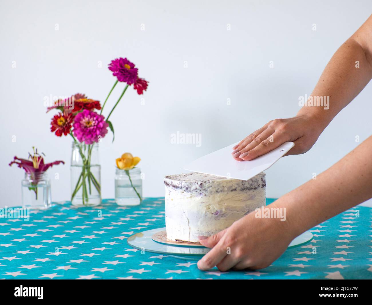 Die Creme mit einem Teigschaber von den Händen abgleichen und den runden Kuchen bedecken Stockfoto