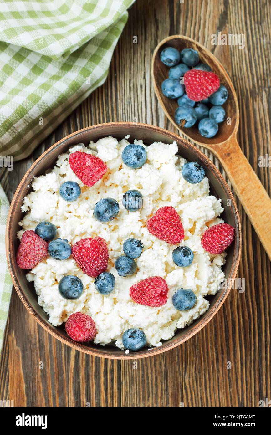 Quark mit Himbeeren und Heidelbeeren in brauner Tonschüssel und Holzlöffel auf braunem Holzhintergrund. Milchprodukte, gesunde Lebensmittel. Flach legen Stockfoto