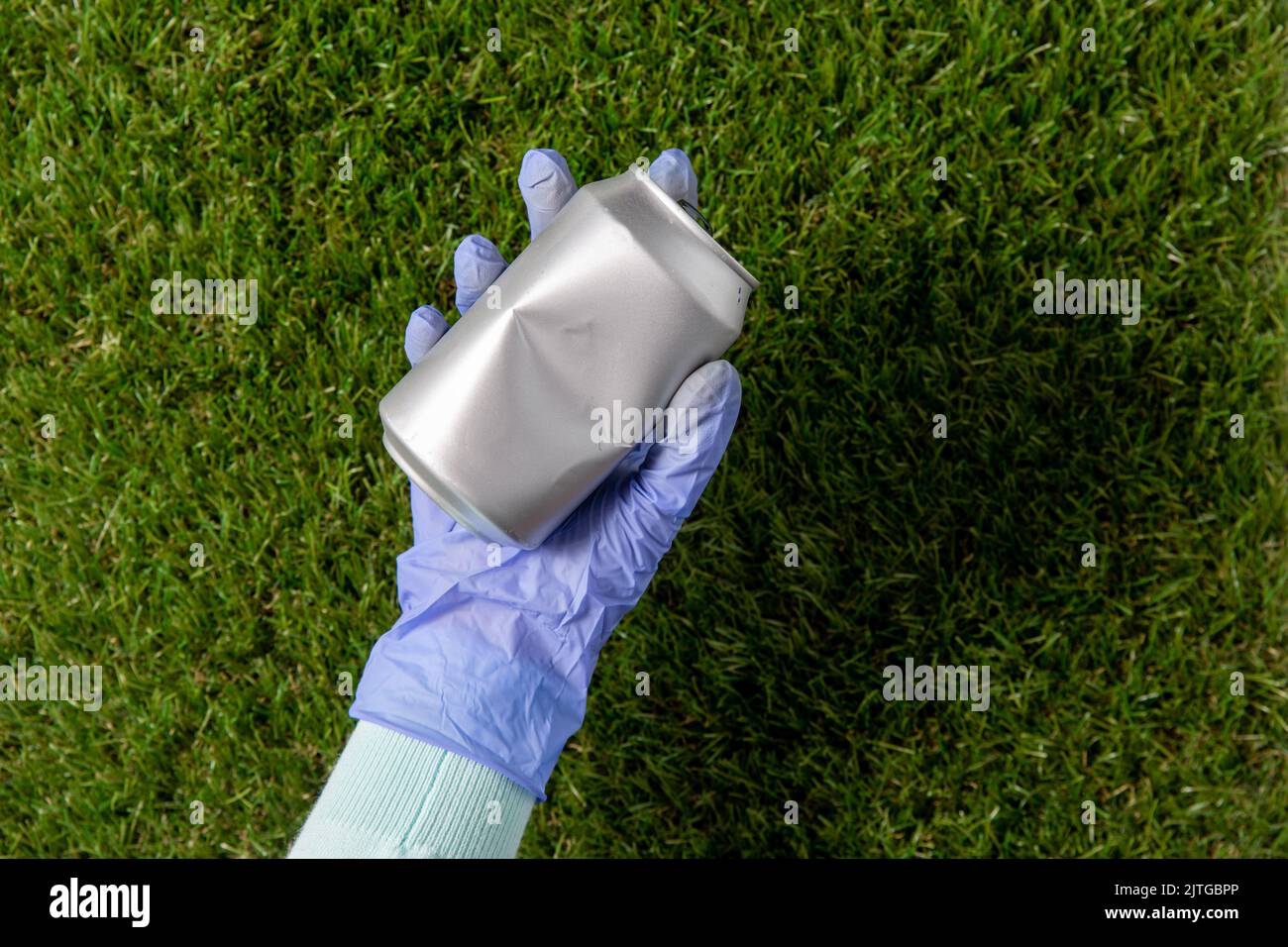Nahaufnahme der Hand im Handschuh mit gebrauchter Dose auf Gras Stockfoto