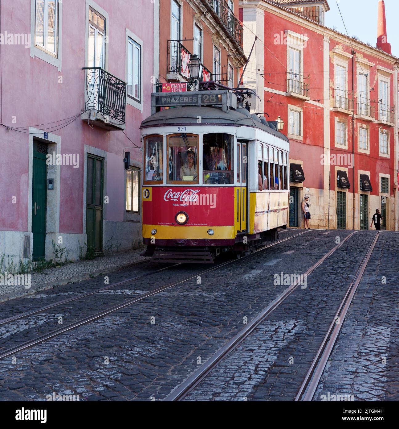 Rote und gelbe Straßenbahn (auch bekannt als Trolley oder Straßenbahn) in Lissabon mit rosa und roten Gebäuden hinter dem Hotel an einem Sommerabend. Portugal Stockfoto