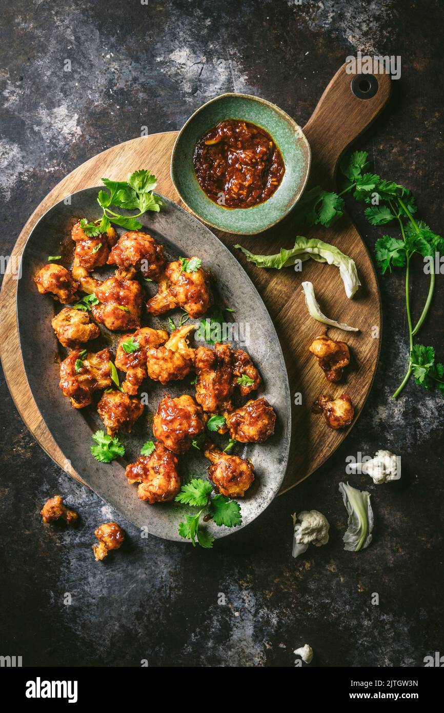 Gebratene, zerfetzte gewürzte Blumenkohlröschen auf einer Platte mit Sauce und Petersilie garnieren Stockfoto