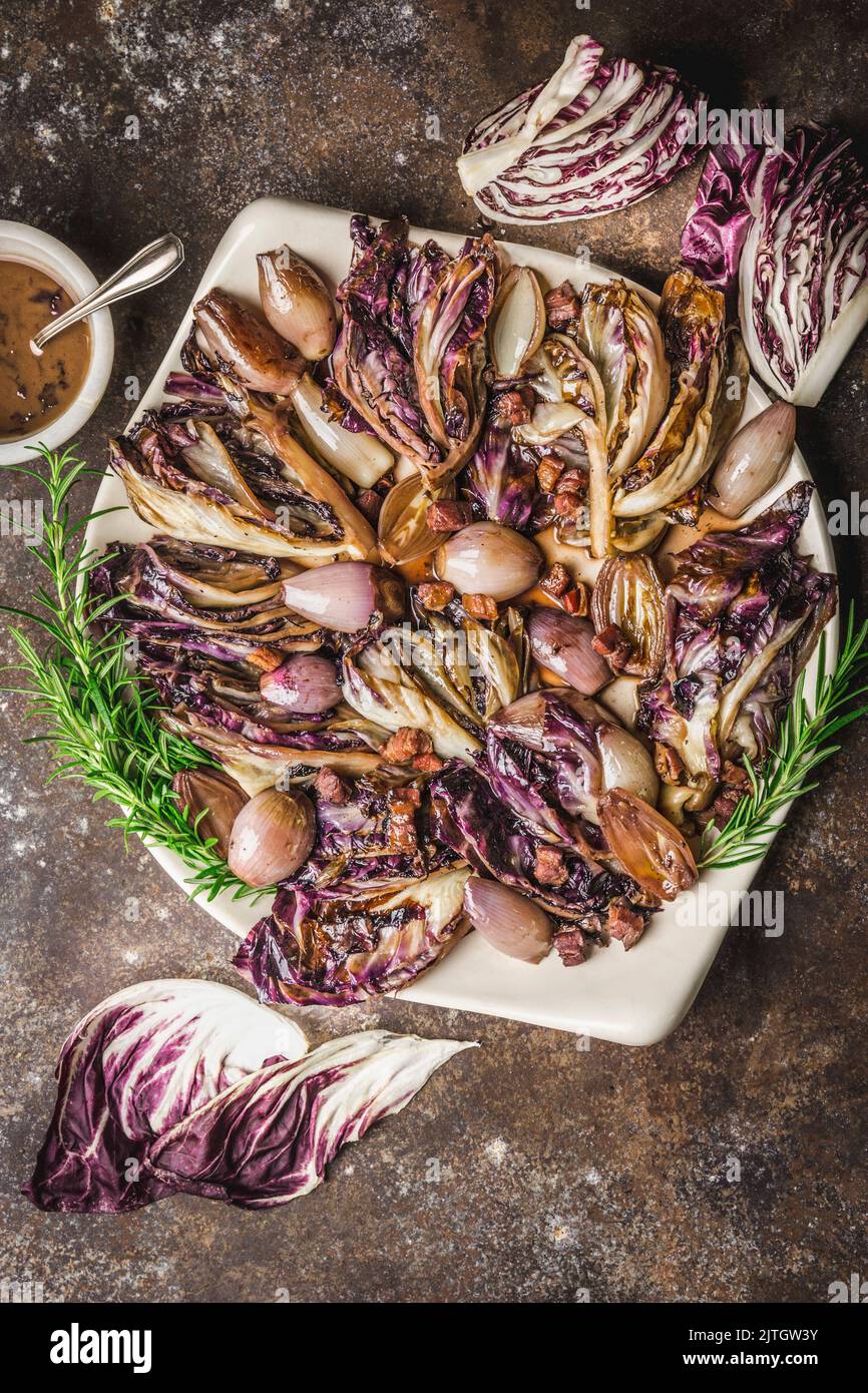 Geschmorte Radicchio und Schalotten auf Servierplatte mit Soßenschüssel und Rosmarin-Garnitur Stockfoto