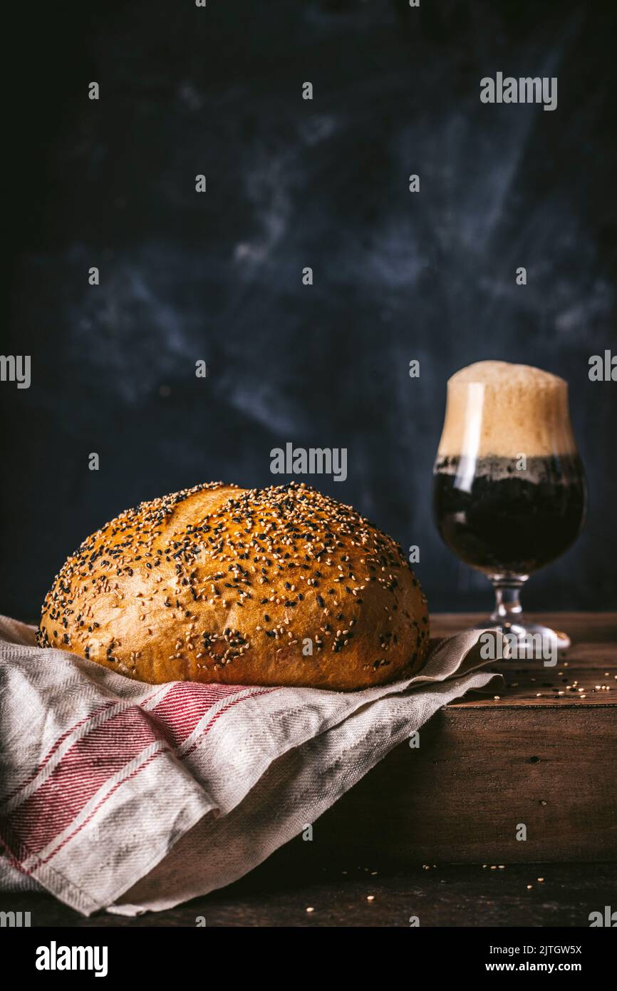 Runder Brot-Moppyseed-Laib mit dunklem schaumigem Bier im Glas Stockfoto
