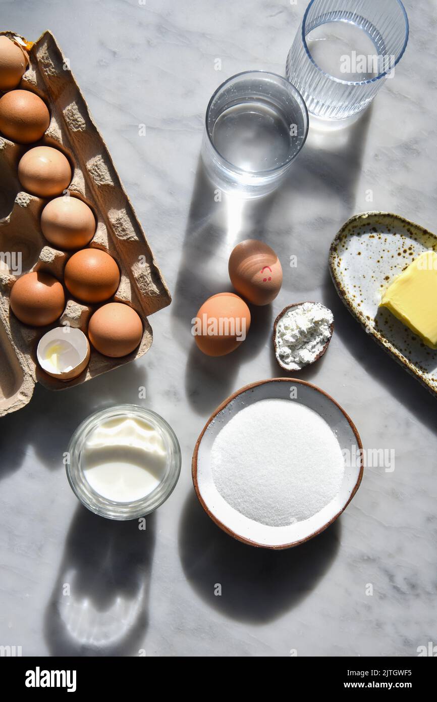 Backzutaten im Sonnenlicht, darunter Eier, Mehl, Zucker und Butter Stockfoto