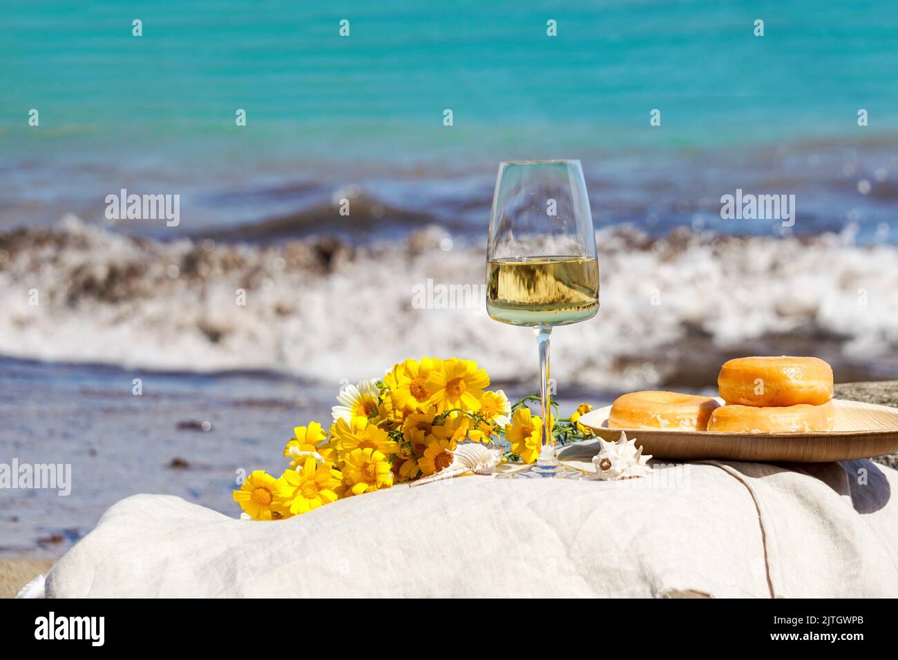 Glas mit Weißwein auf Steinhockern vor blauem Meer und Wellen, Sommer-Picknick-Konzept Stockfoto