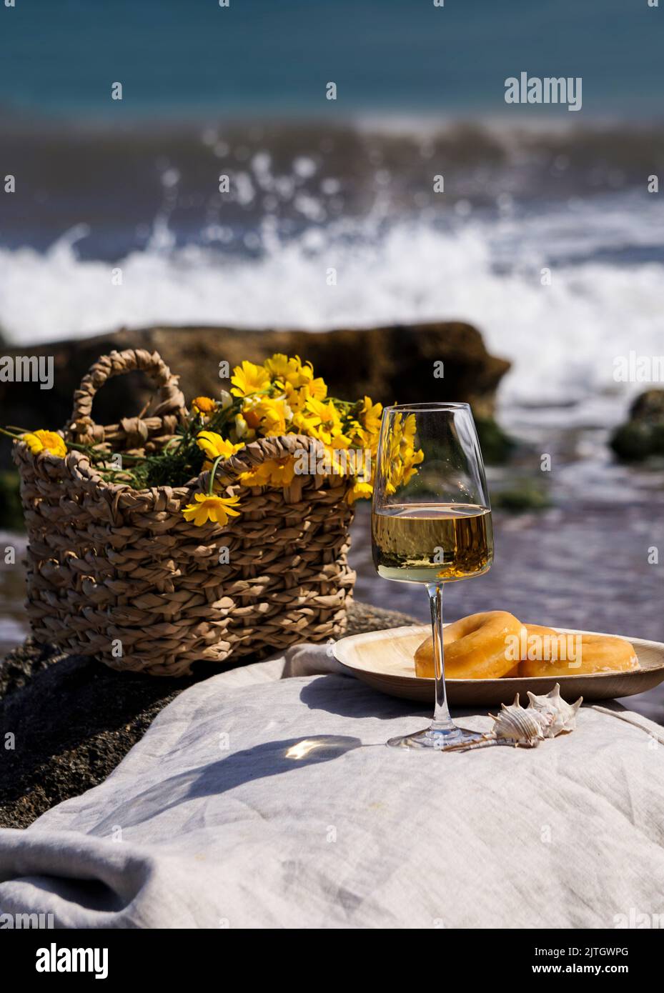 Glas mit Weißwein auf Steinhockern vor blauem Meer und Wellen, Sommer-Picknick-Konzept Stockfoto