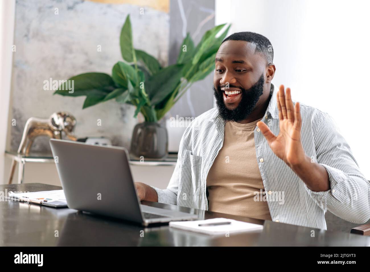 Online-Videogespräche. Ein positiv freundlicher afroamerikanischer Mann, Vertriebsleiter, Kreativmanager, sitzt im Büro, führt per Videoanruf mit Kollegen über einen Laptop ein lachend Geschäftsgespräch Stockfoto