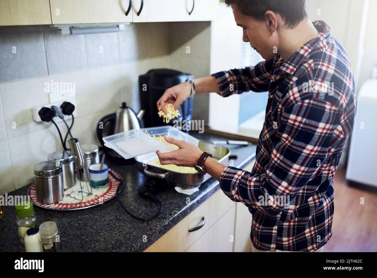 Hinzufügen von etwas Käse für zusätzlichen Geschmack. Ein hübscher junger Mann Kochen in der Küche zu Hause. Stockfoto