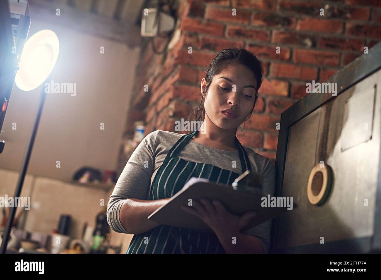 Sie notiert jedes Detail in ihrem Geschäft. Eine junge Unternehmerin, die in einem Workshop auf einem Clipboard schreibt. Stockfoto