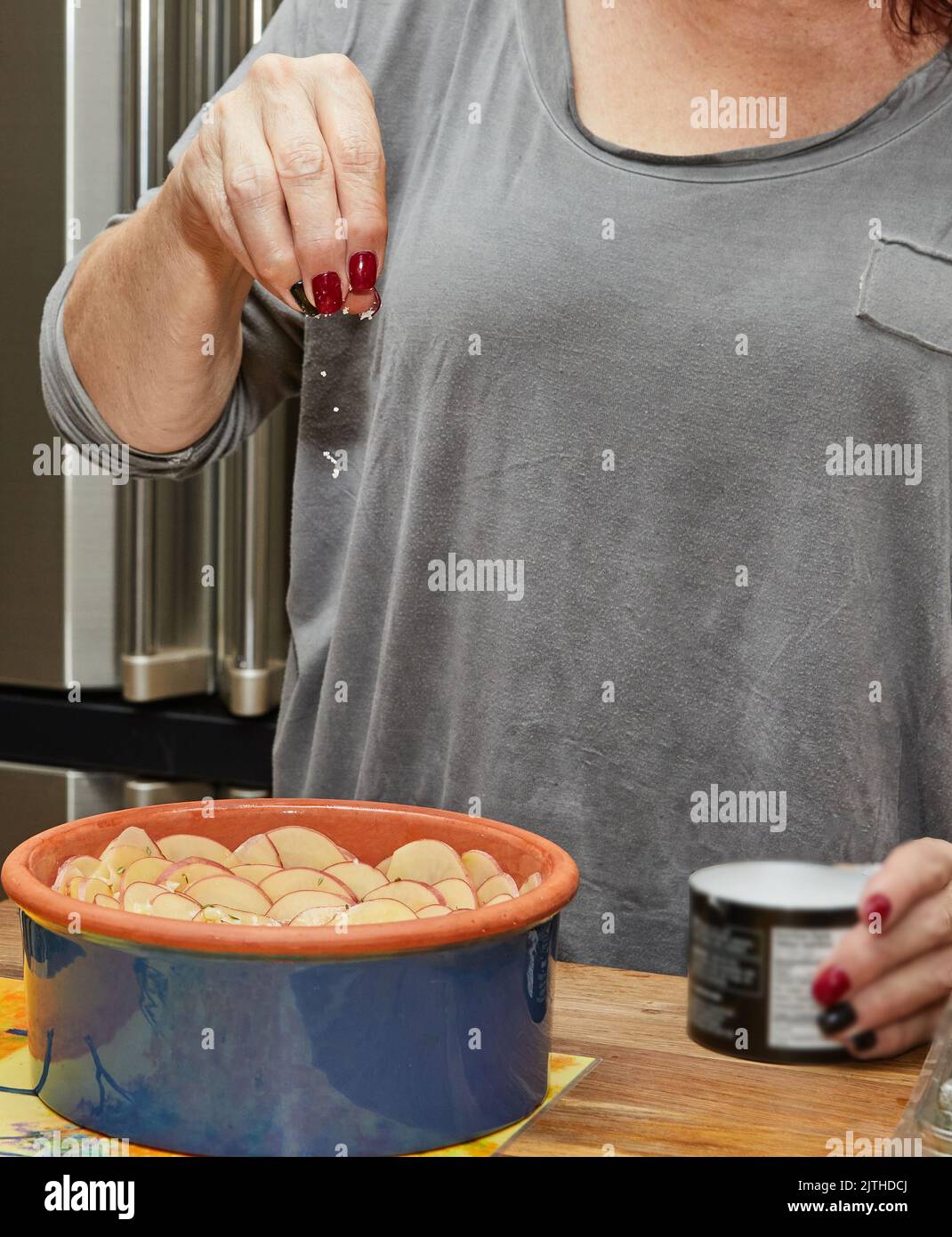Chefkoch salzt Kartoffelgratin in einer blumenförmigen Keramikschale Stockfoto
