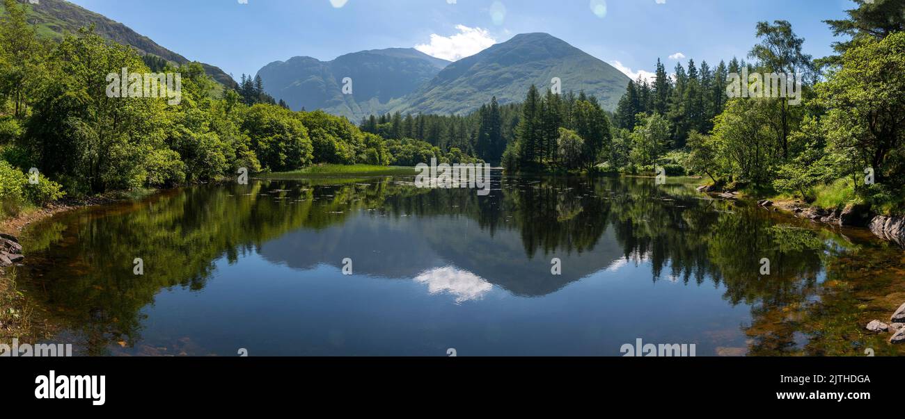 Glen Coe in der Lochaber-Gegend der schottischen Highlands.entfernte Berge spiegeln sich in den stillen Gewässern eines ruhigen, in einem Waldsee an einem heißen Sommer Stockfoto