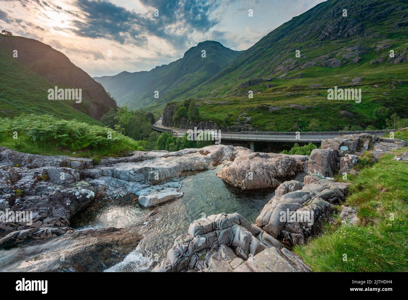 Die untergehende Sonne, über dem dramatischen Tal von Glen Coe, im Sommer, wo sich drei kleine Flüsse treffen, am Fuße der Three Sisters of Glen Coe, mit AW Stockfoto