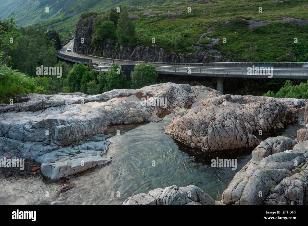 Die untergehende Sonne, über dem dramatischen Tal von Glen Coe, im Sommer, wo sich drei kleine Flüsse treffen, am Fuße der Three Sisters of Glen Coe, mit AW Stockfoto