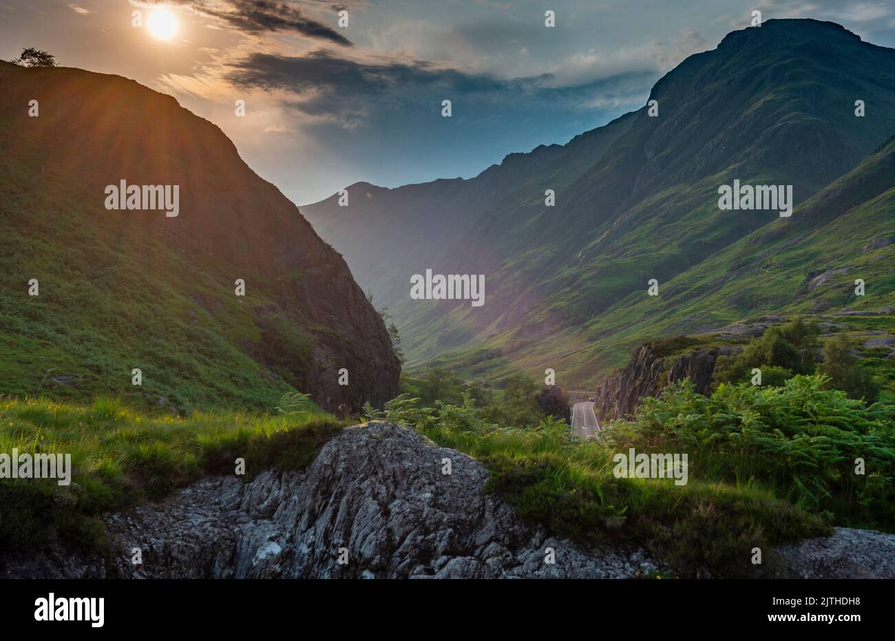 Die Lichtstrahlen der untergehenden Sonne, über dem dramatischen Tal von Glen Coe, im Sommer, wo sich drei kleine Flüsse treffen, verläuft die Hauptstraße entlang des Tals i Stockfoto