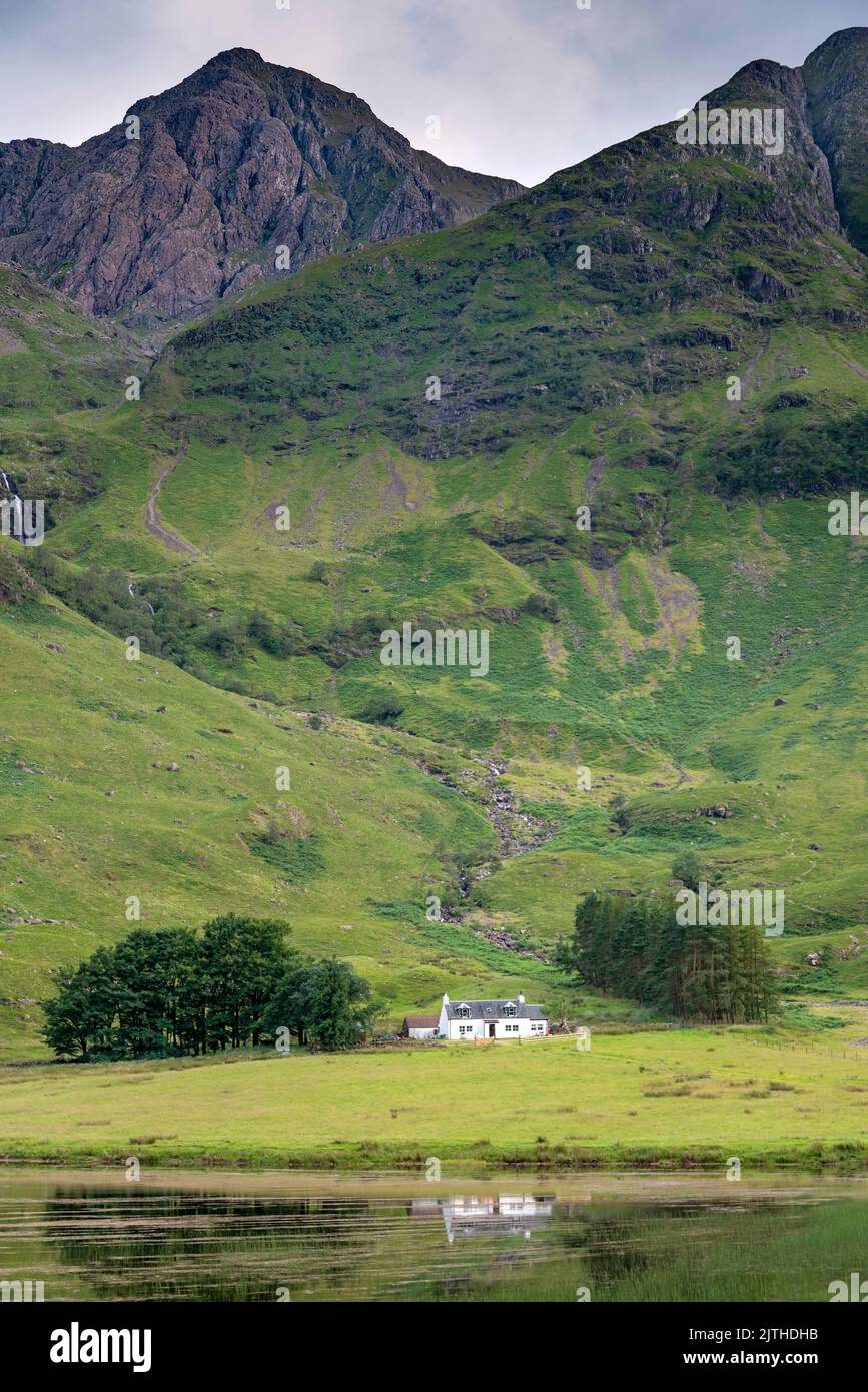 In Lochaber, umgeben von den majestätischen Bergen entlang des Tals von Glencoe, liegt das kleine malerische Häuschen zwischen einem Baumkronen, der von wanderwegen genutzt wird Stockfoto