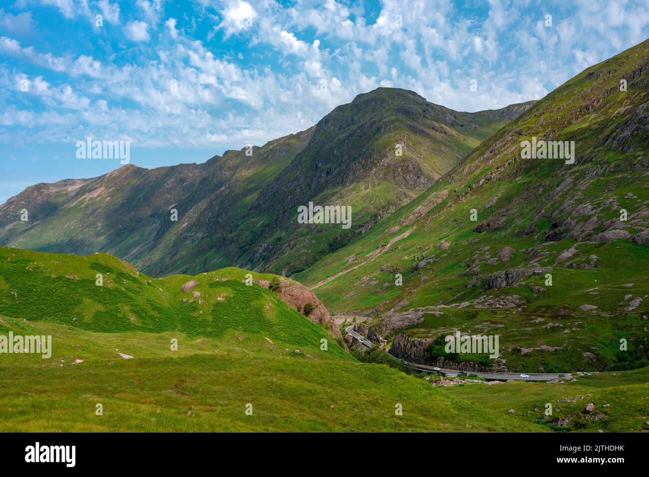 Schön, Bereich der Highlands, bedeckt mit grünem Sommerrasen, blauer Himmel oben. Die Straße schlängelt sich zwischen der herrlichen Landschaft, beliebt bei Touristen, hallo Stockfoto