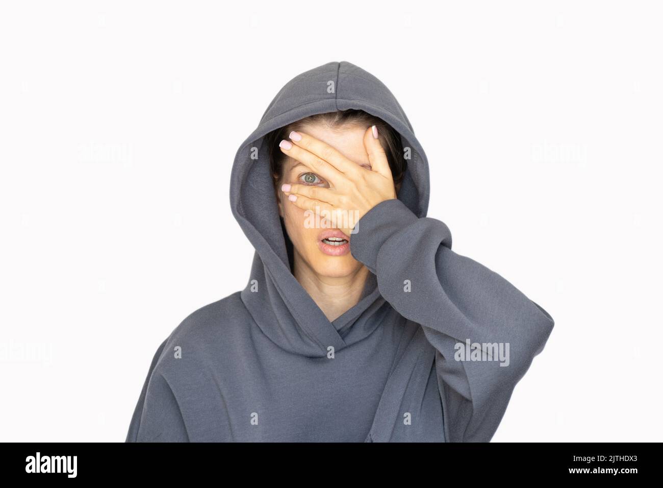 Ein Mädchen in einem Trainingsanzug schließt ein Auge mit ihrer Hand auf weißem Hintergrund, schau durch ihre Hand, ich sehe Stockfoto