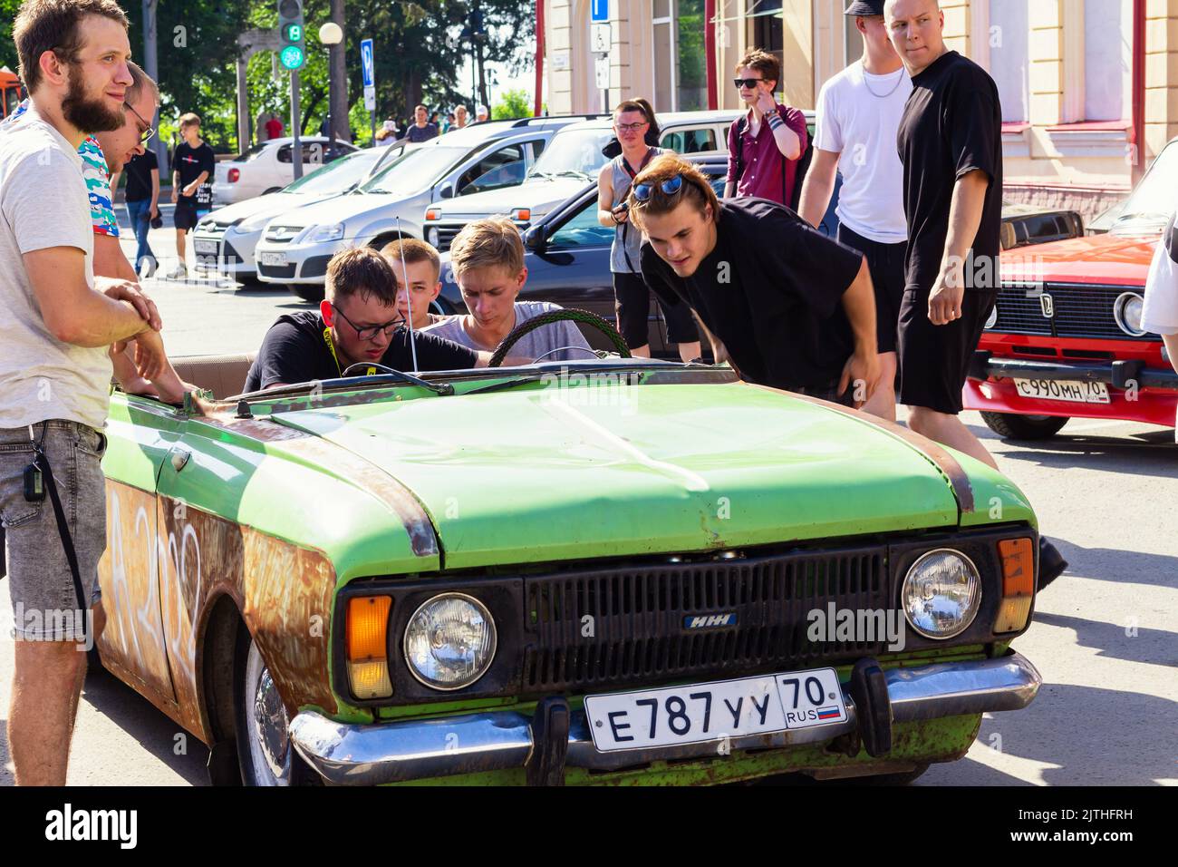 Altes schäbiges Auto IZH blieb mitten auf der Straße stecken. Der öffentliche Verkehr ist zusammengebrochen. Tomsk Russland 26 2022. Juni, Jugendtag Menschen helfen, Auto zu reparieren.Transport Co Stockfoto